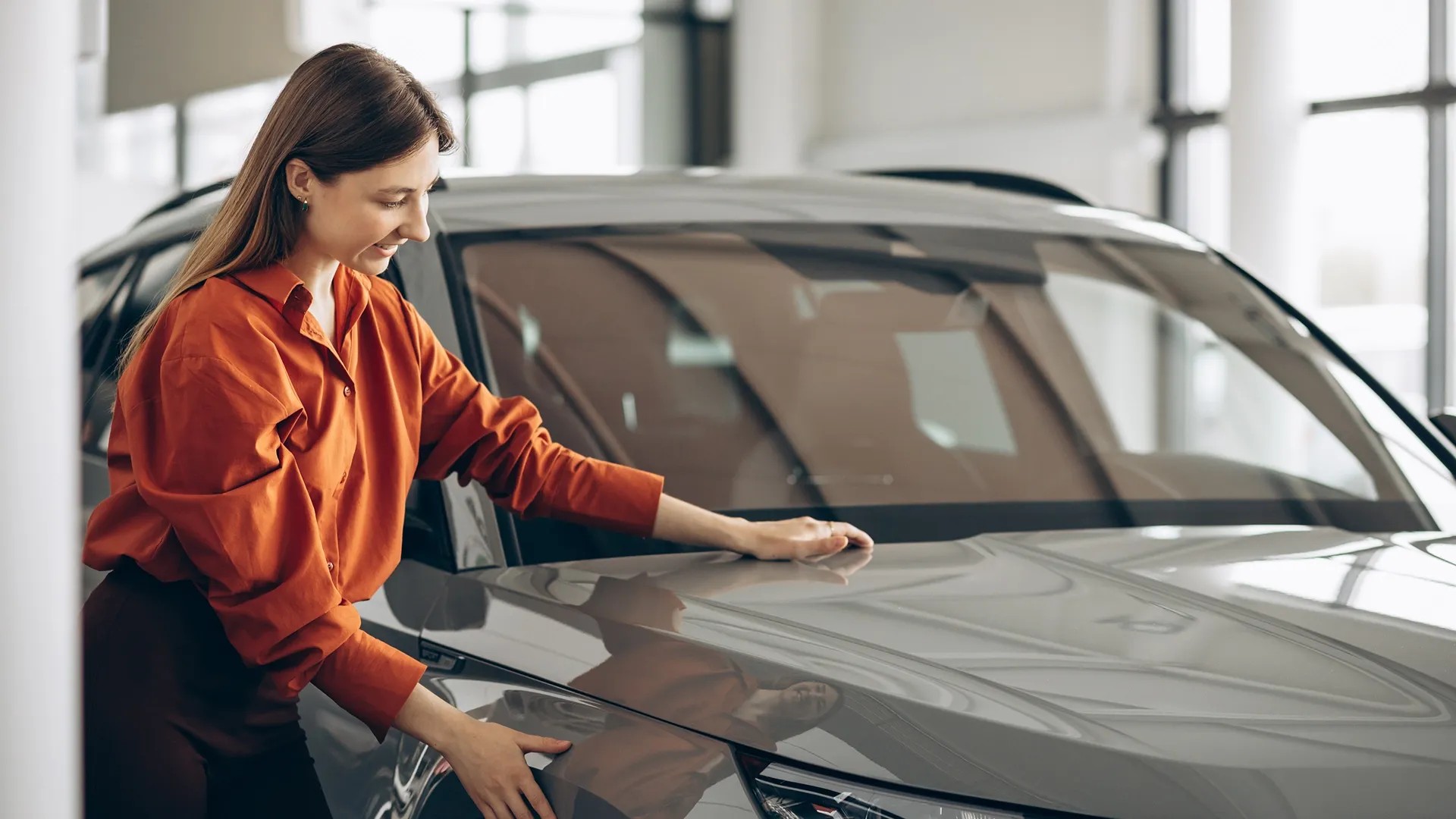 A woman is inspecting a car in the showroom