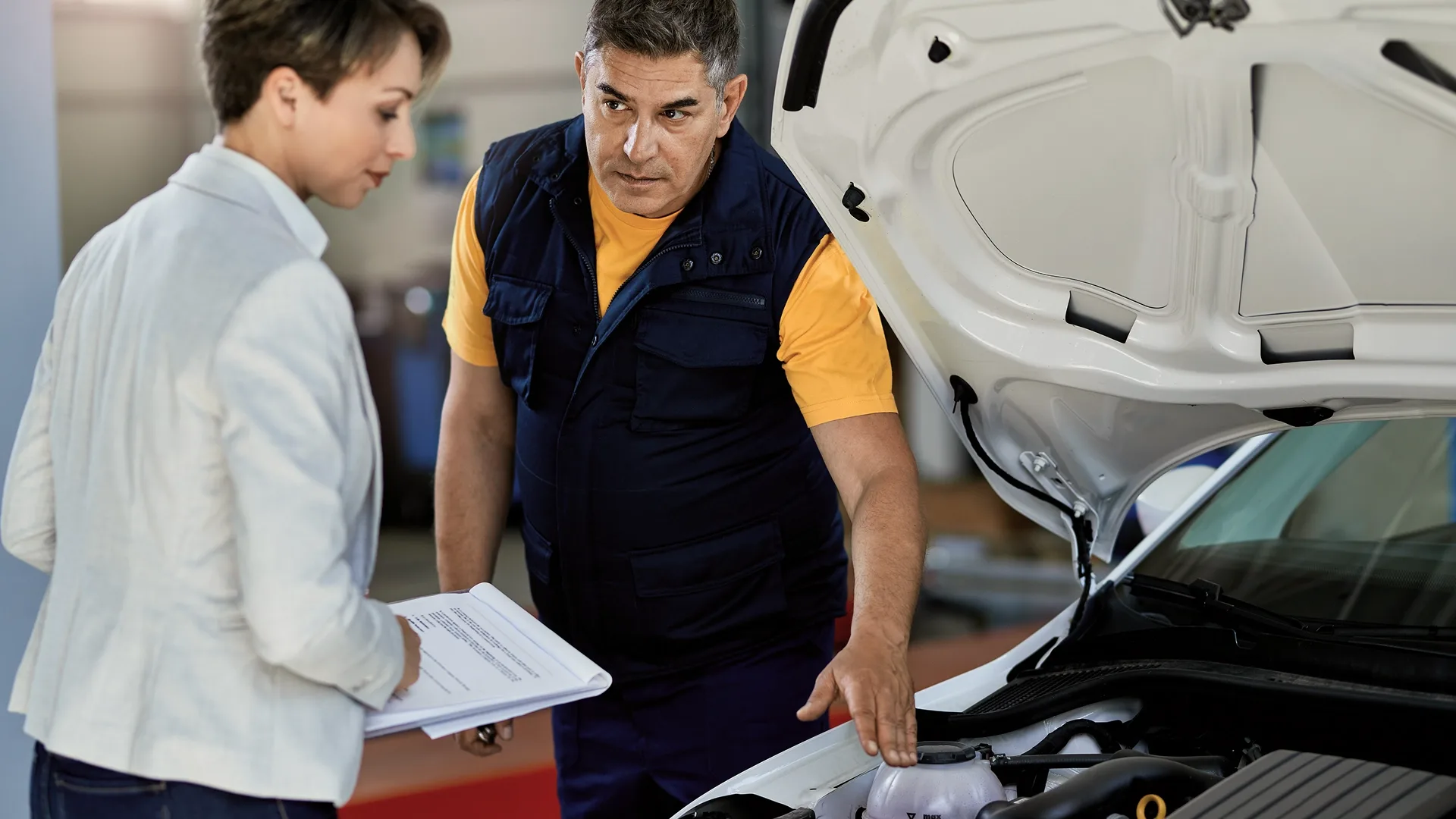 Mechanic inspecting a used car with a potential buyer after an accident